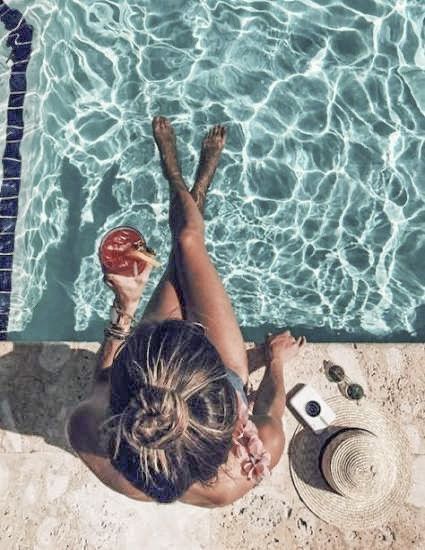 a woman laying on the ground next to a swimming pool with a drink in her hand