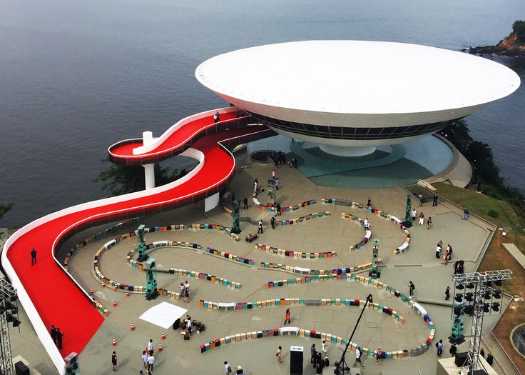 an aerial view of a building with many people around it and water in the background