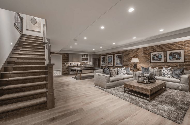 a living room filled with furniture next to a stair case in front of a brick wall