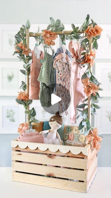 a wooden crate filled with baby clothes on top of a white table next to framed pictures