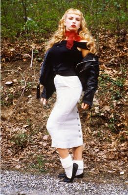 a woman in a white skirt and black jacket is walking down the road with her hands on her hips