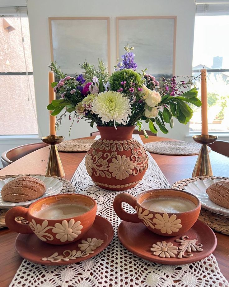 the table is set with two cups and saucers, one has flowers in it