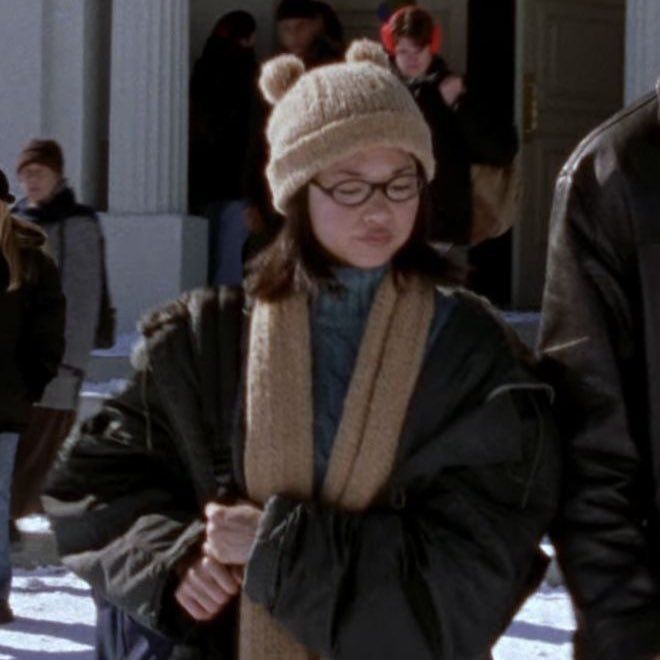 a woman wearing a hat and scarf walking in the snow with other people behind her