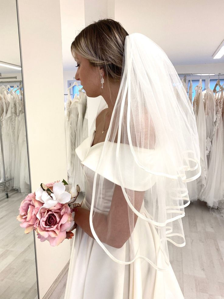 a woman in a wedding dress looking at herself in the mirror with her veil over her head