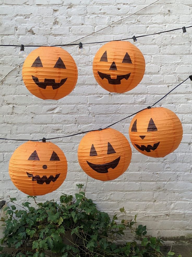 four pumpkin lanterns hanging from a string on a brick wall