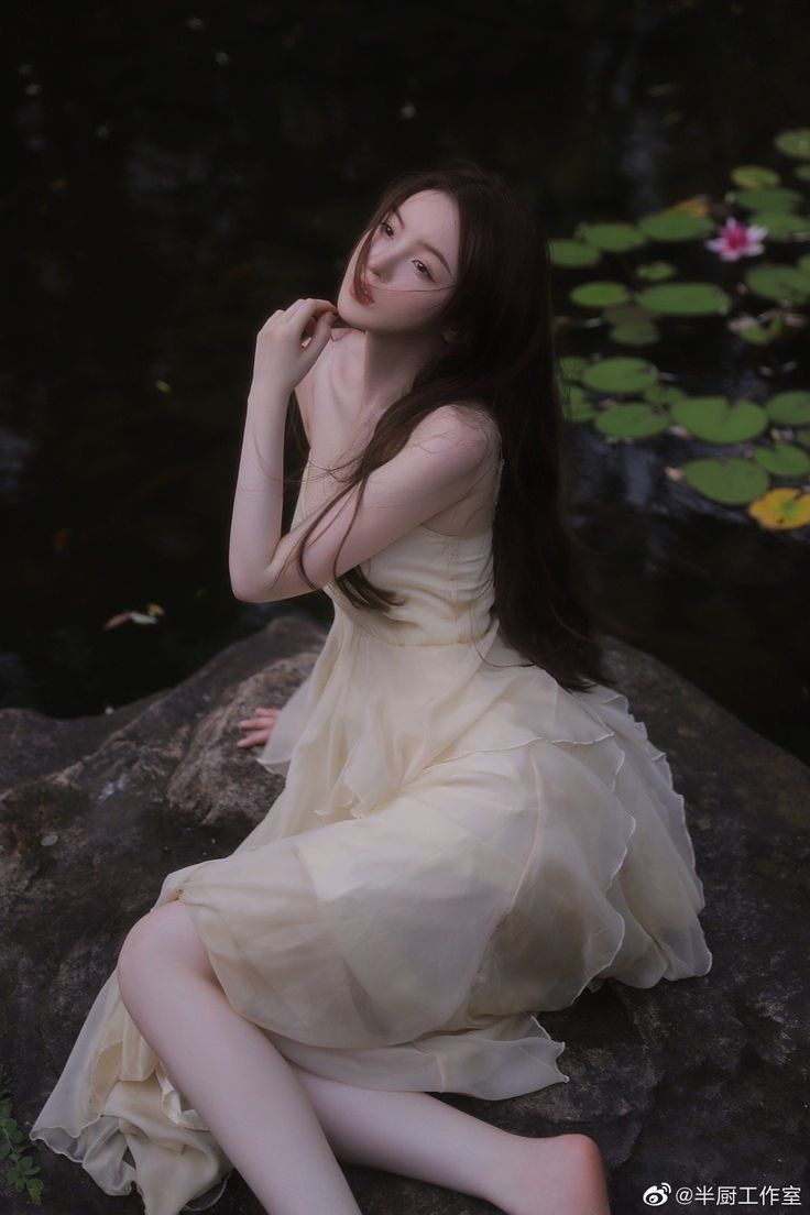 a woman sitting on top of a rock next to a body of water with lily pads