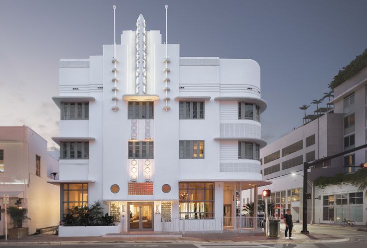 the building is white with many windows and people walking around in front of it at dusk