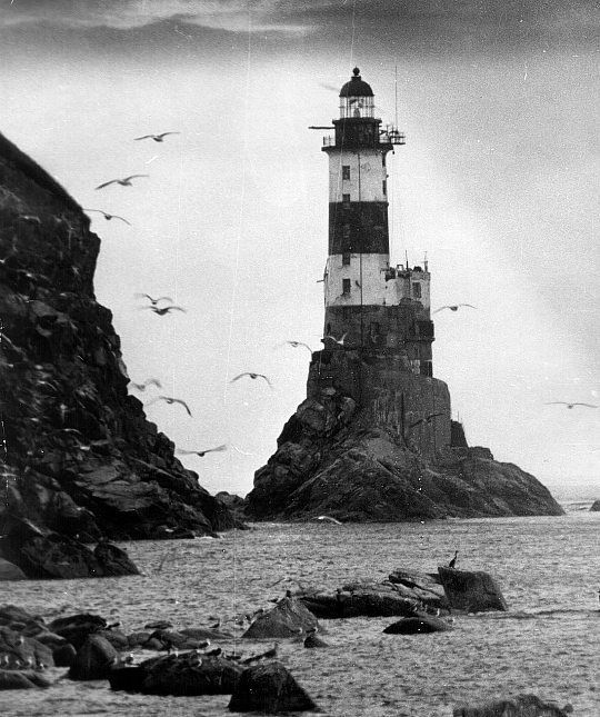 an old photo of a lighthouse in the ocean with seagulls flying around it