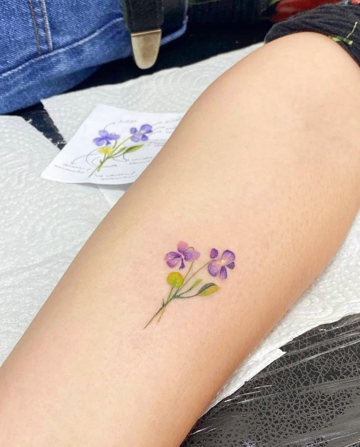 a woman's leg with purple and yellow flowers tattooed on the left side of her arm