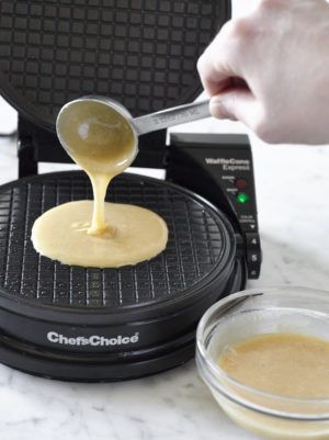 a person using a spoon to pour sauce on a waffle maker