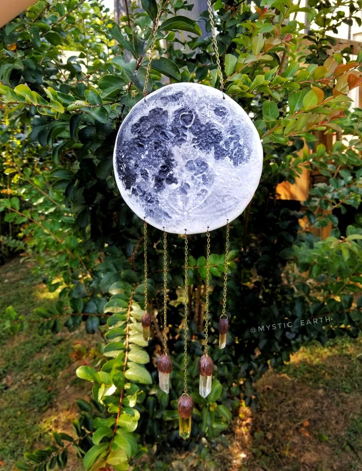 a wind chime hanging from a tree in the grass with leaves and flowers around it