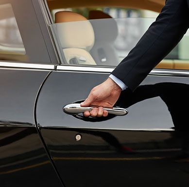 a man in a suit opens the door of a car with his hand on the handle