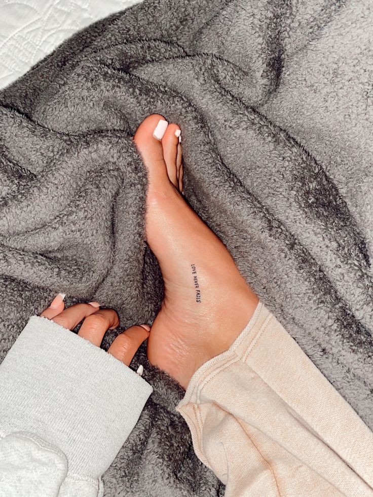 a woman's bare feet with tattoos on them laying on a gray and white blanket