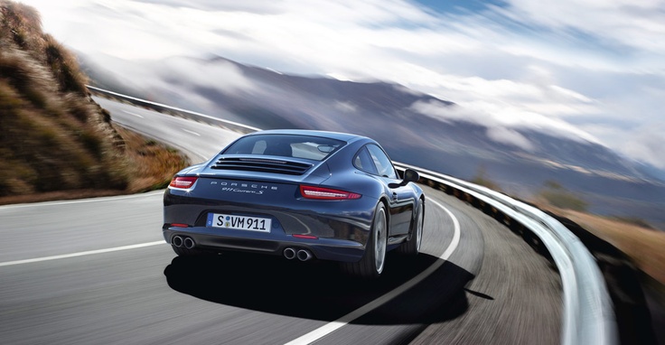 a grey sports car driving down the road with mountains in the backgrouund