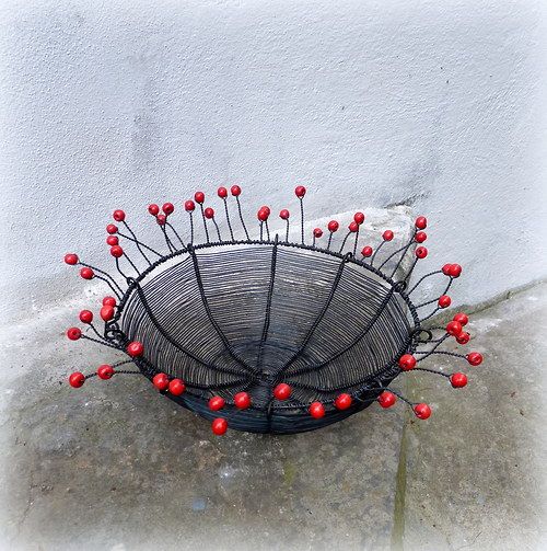 a wire basket with red berries on it sitting in front of a white stucco wall