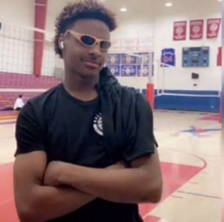 a young man with his arms crossed standing in front of a basketball court wearing sunglasses