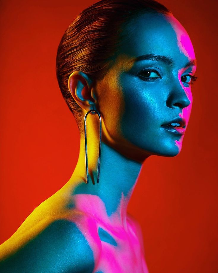 a woman with bright blue and pink paint on her body, wearing large gold hoop earrings