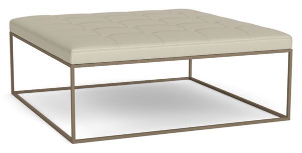 a white ottoman sitting on top of a metal frame with a beige leather cushion underneath it