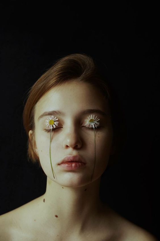 a woman with two daisies on her face and one flower sticking out of her nose