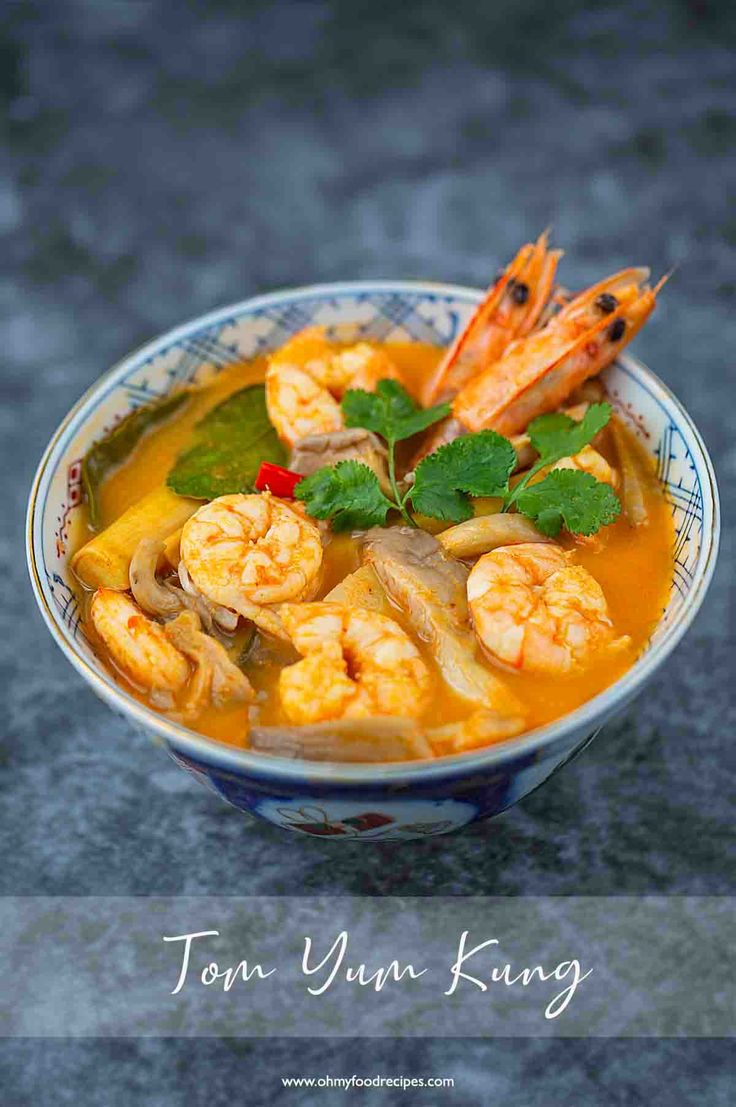 a blue and white bowl filled with shrimp, noodles and carrots in broth