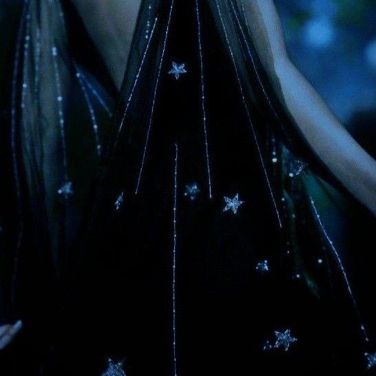 a woman with long black hair and stars on her dress is looking at the camera