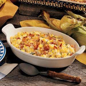 corn casserole with bacon and cheese in a white dish next to corn on the cob