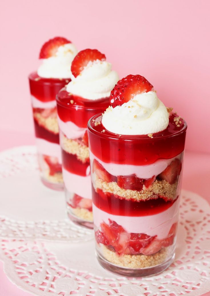 three desserts with strawberries and whipped cream in them on a white doily