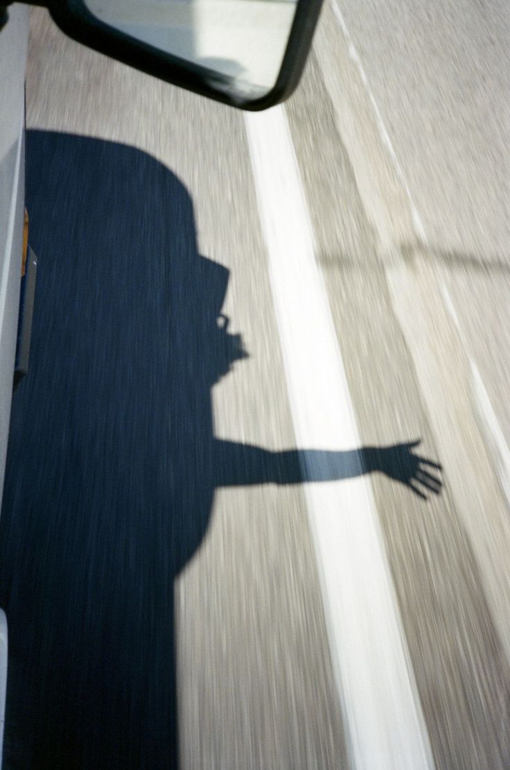 the shadow of a person is seen on the side mirror of a vehicle as it drives down a street