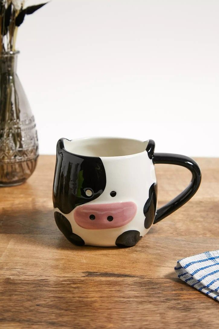 a black and white cow mug sitting on top of a wooden table next to a vase