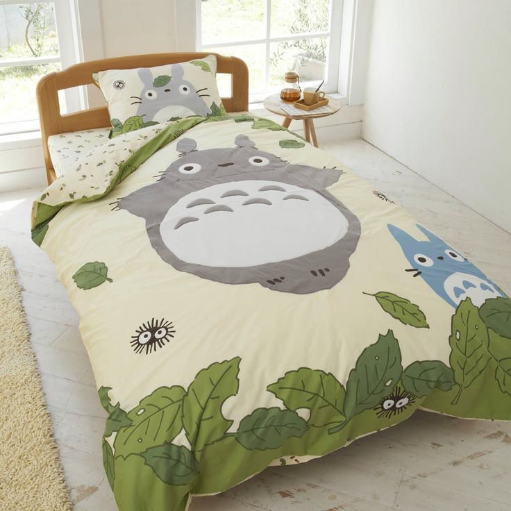 a bed with a totoro print on it and green leaves around the comforter