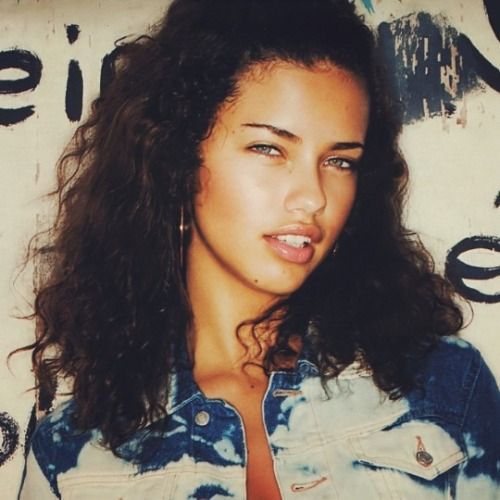 a close up of a person wearing a jean jacket and posing for a photo with graffiti on the wall behind her