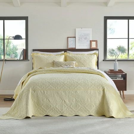 a bed with yellow bedspread and pillows in a bedroom next to two windows