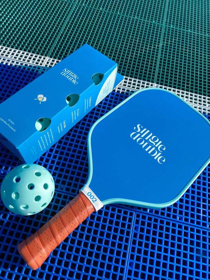 two ping pong paddles and a ball on a blue tablecloth next to a box