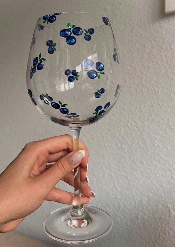 a hand holding a wine glass with blue flowers on it