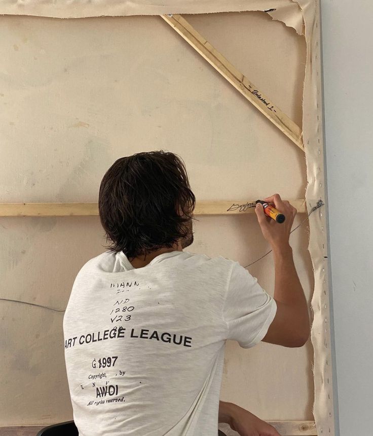 a man in white shirt painting on wall with paint rollers and tape measure stick