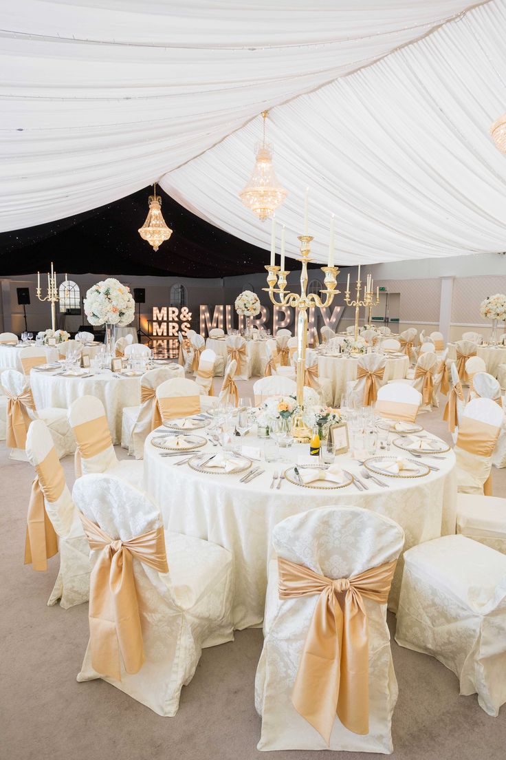 the tables are set up with white linens and gold sashes