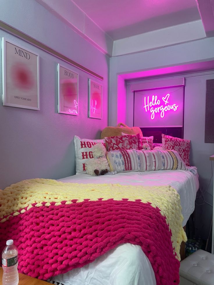 a bed with pink and yellow blankets in a room that has pictures on the wall