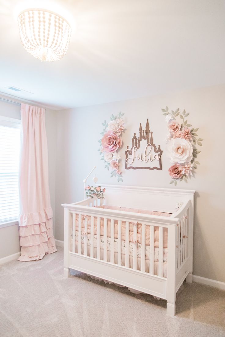 a baby's room with a crib, chandelier and pink curtains