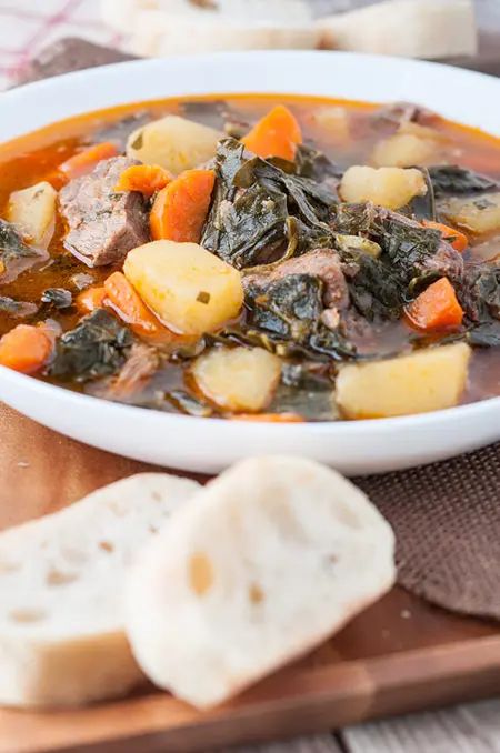 a white bowl filled with stew next to slices of bread