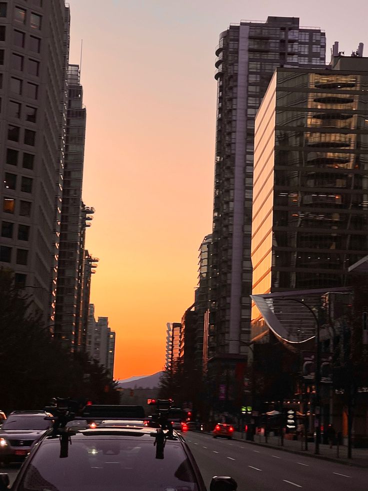 the sun is setting behind tall buildings in an area with cars parked on the street