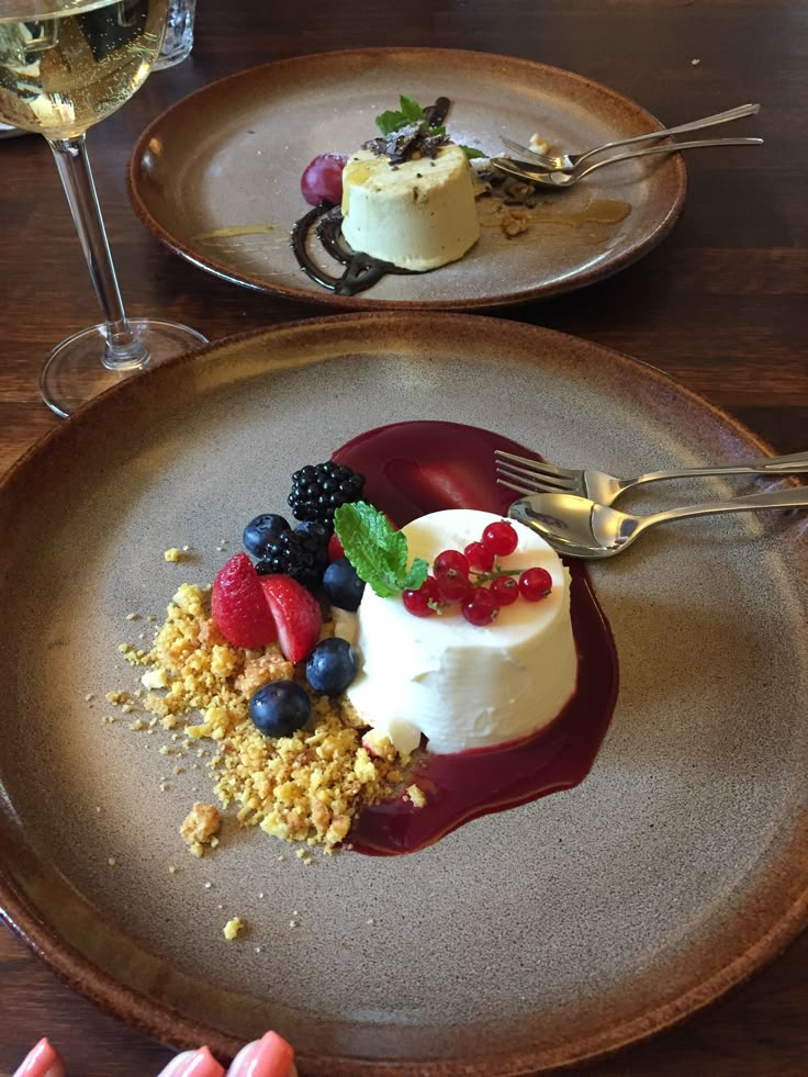 two plates with desserts on them sitting on a table next to glasses of wine