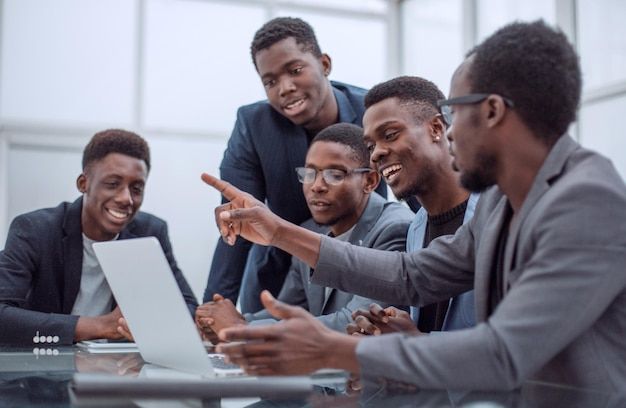 group of men sitting around a laptop pointing at it with one man pointing to the screen