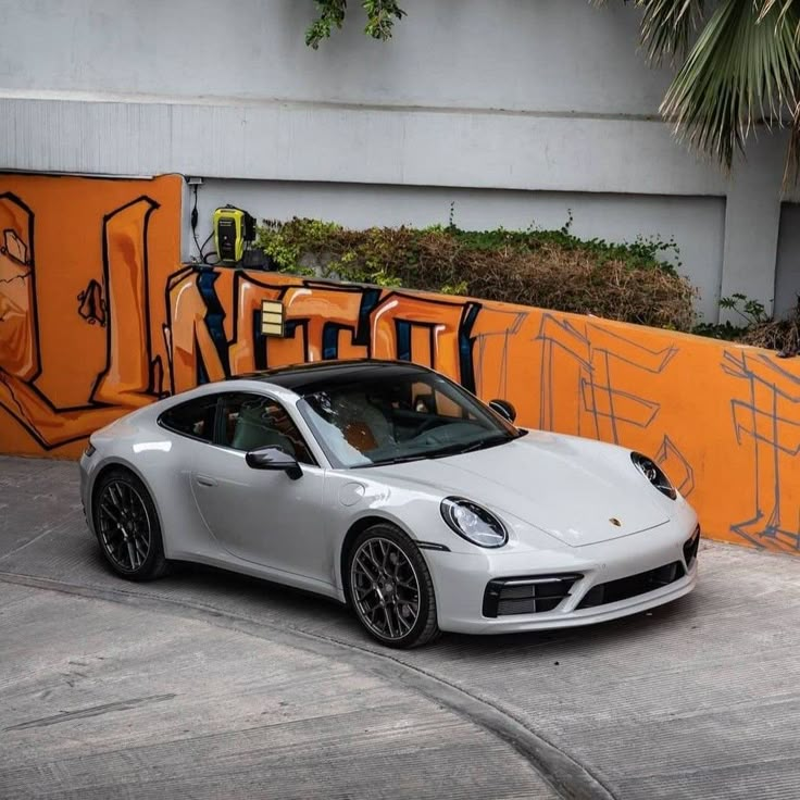 a white porsche parked in front of an orange wall with graffiti on it's side