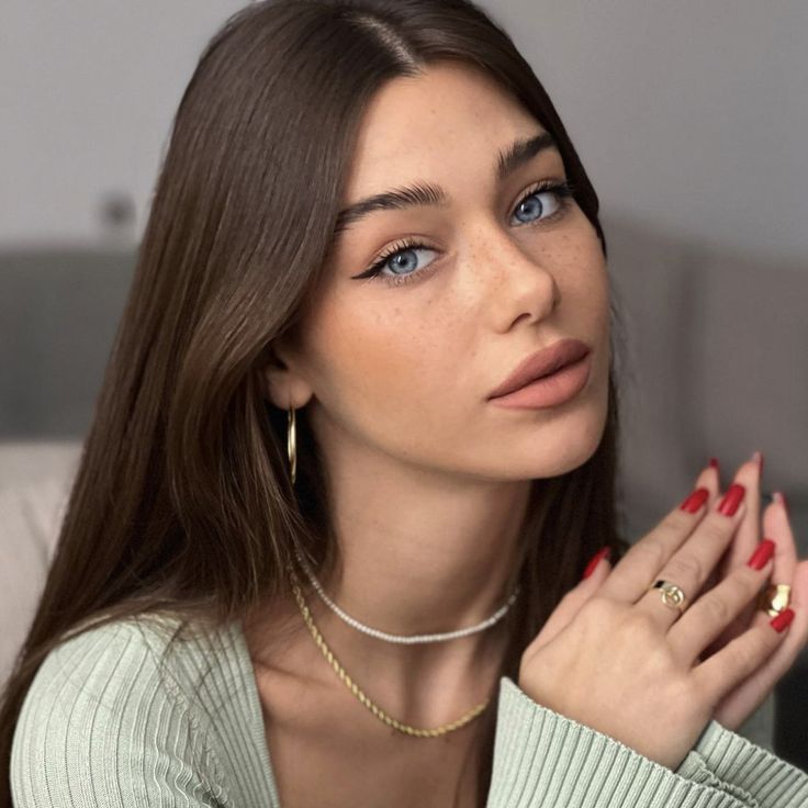 a woman with long brown hair wearing a green sweater and gold rings on her finger