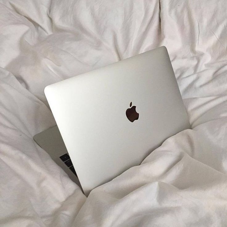 an apple laptop computer sitting on top of a white bed sheet covered in white sheets