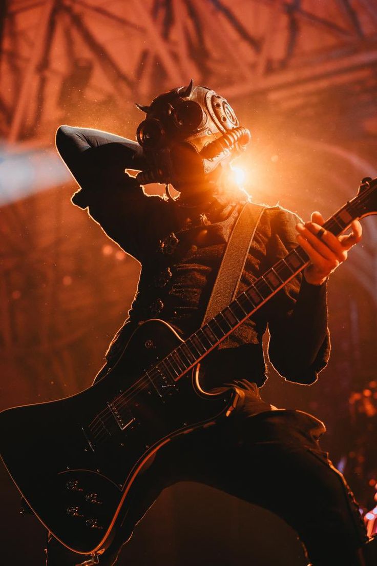 a man with a guitar in his hand and wearing a gas mask on top of his head