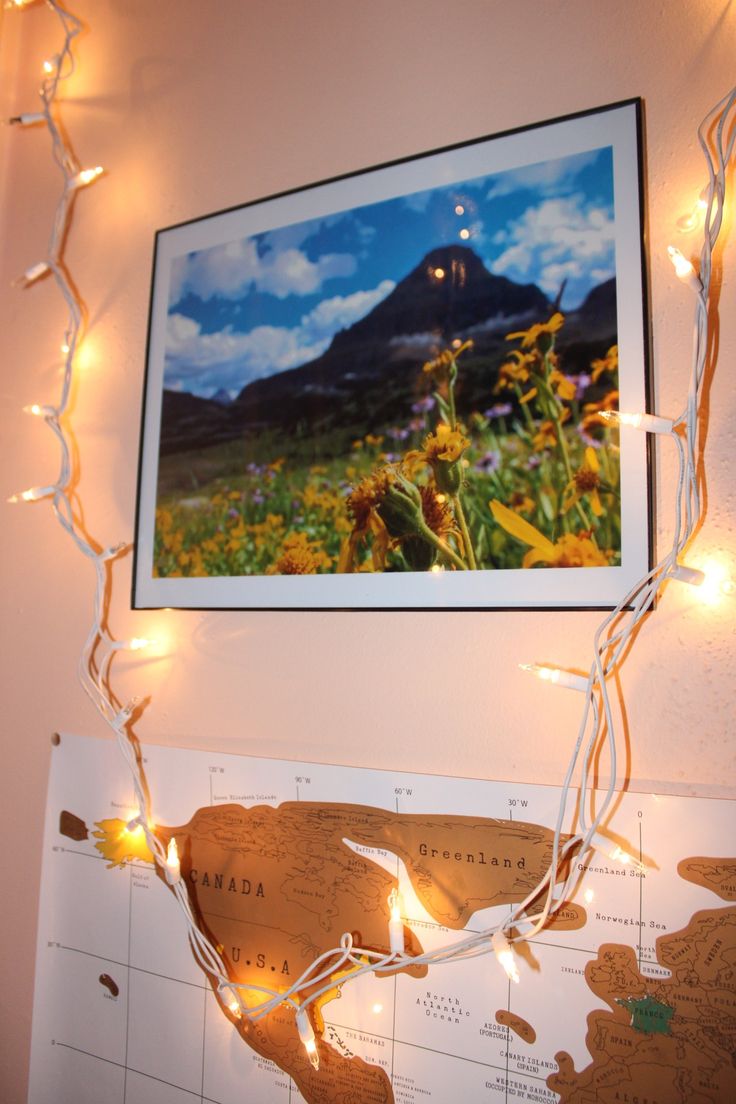 a framed photo hangs on the wall above a map with fairy lights strung around it