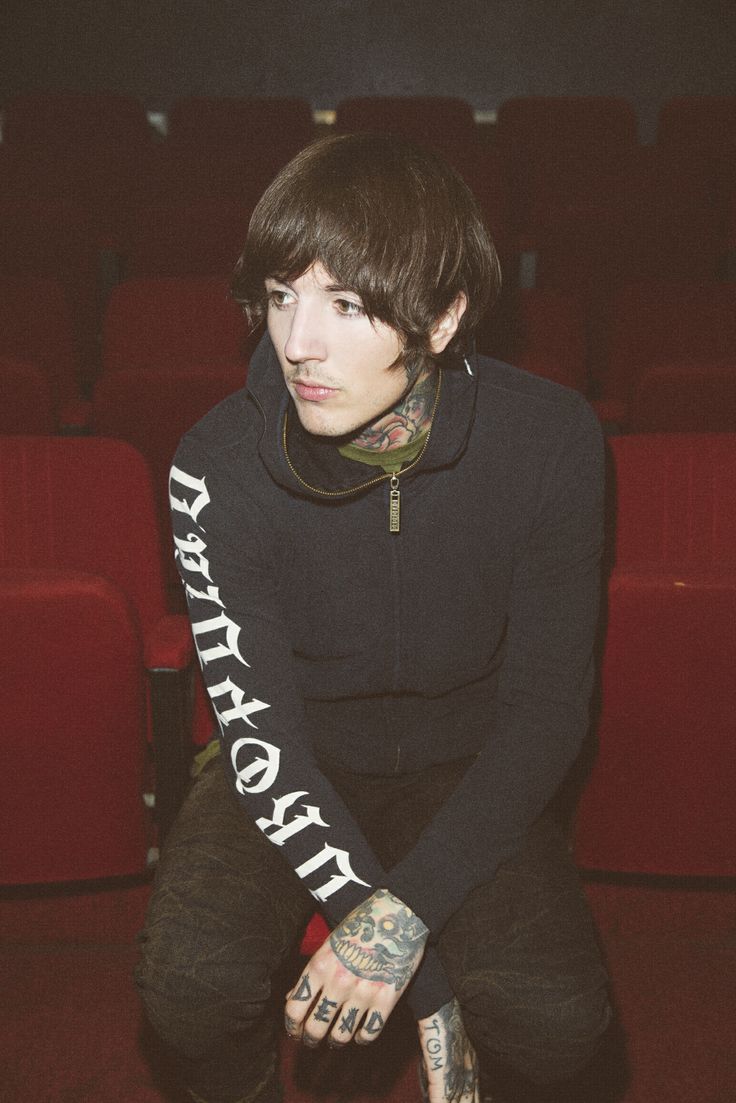 a young man sitting in front of a red chair with his hands on his knees