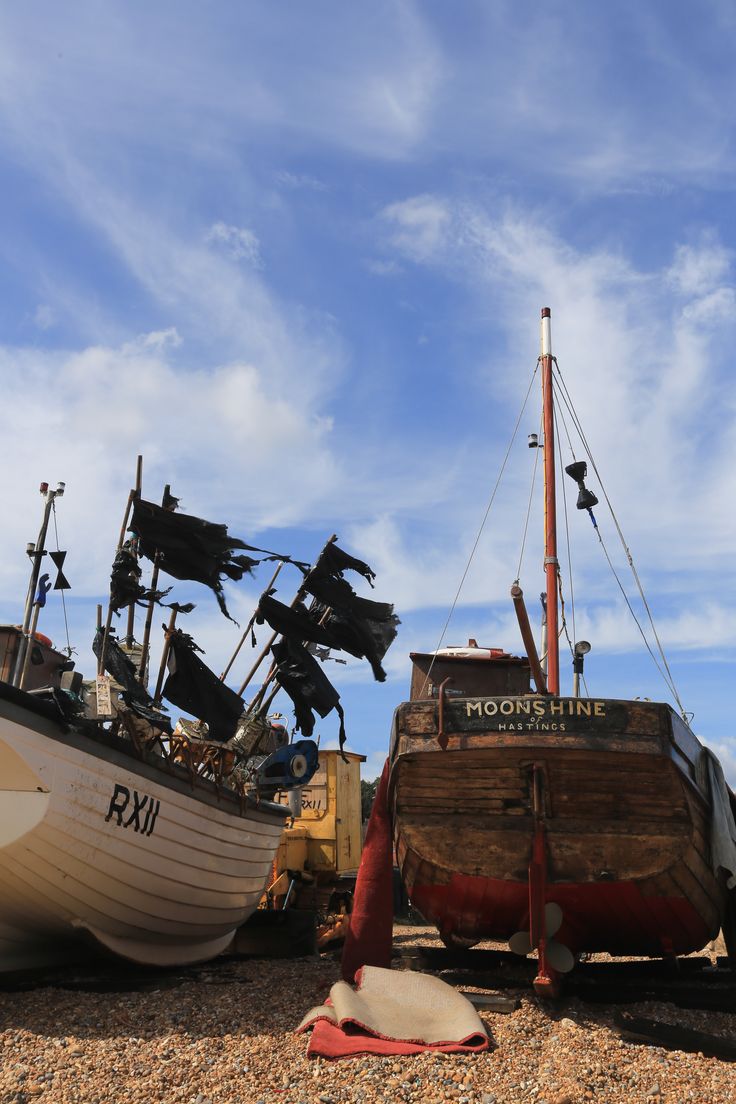 two boats sitting on top of a beach next to each other under a cloudy blue sky