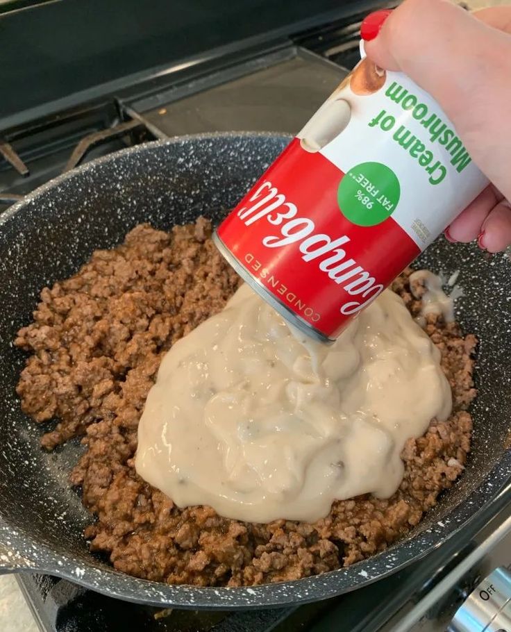 a person pouring mayonnaise into a skillet filled with ground beef